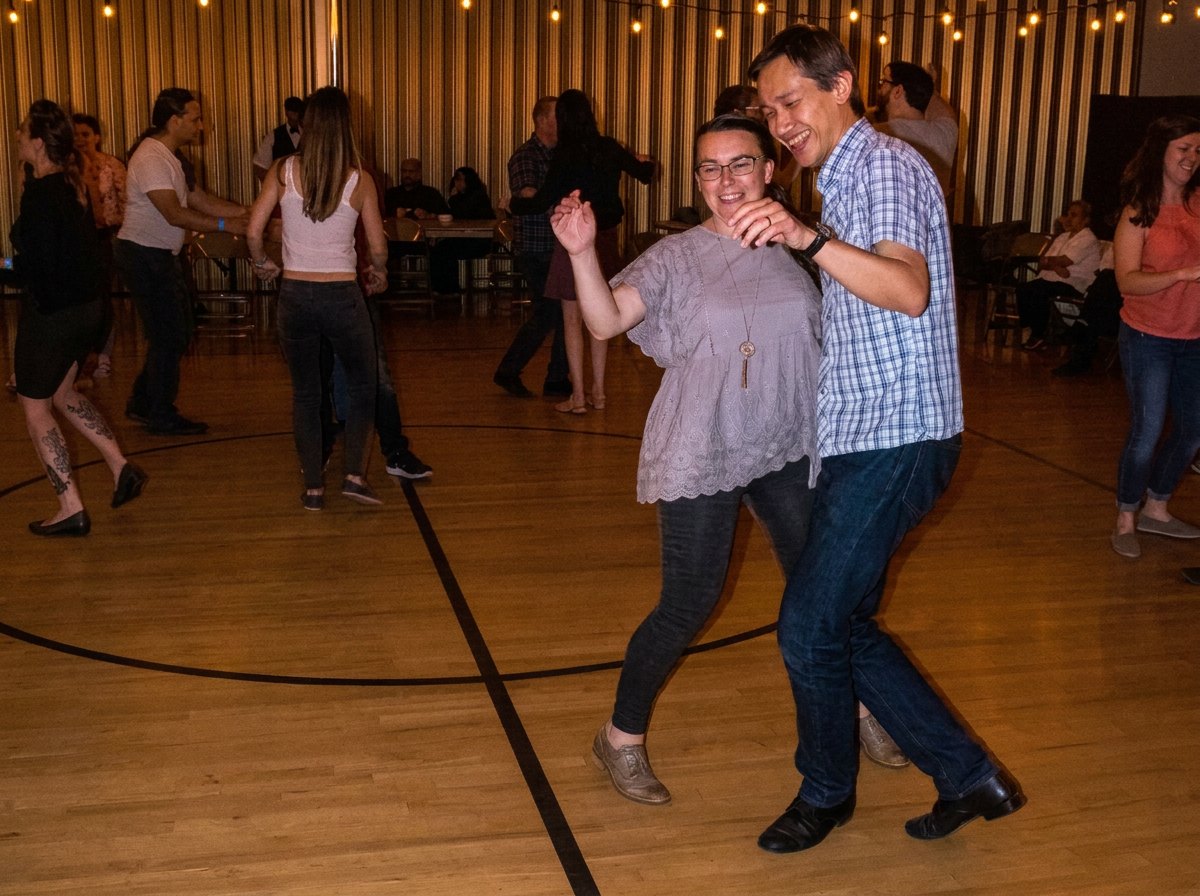 Tan and Adri laughing while swing dancing together at a social dance